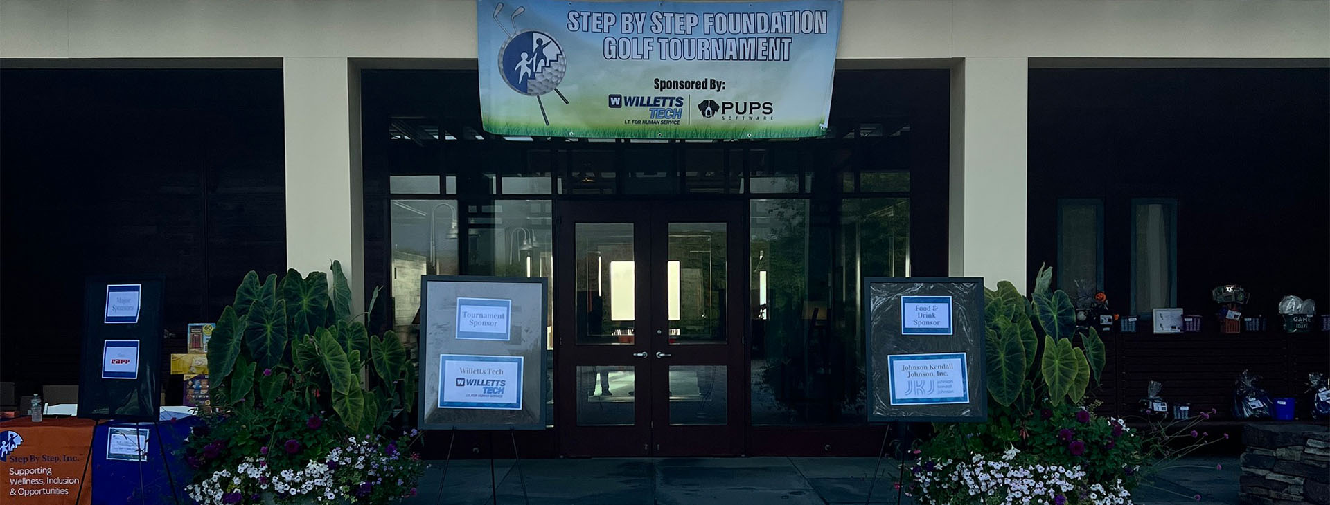 Photo with a banner for the Step by Step Foundation Golf Tournament, sponsored by Willetts Tech and Willetts Pups